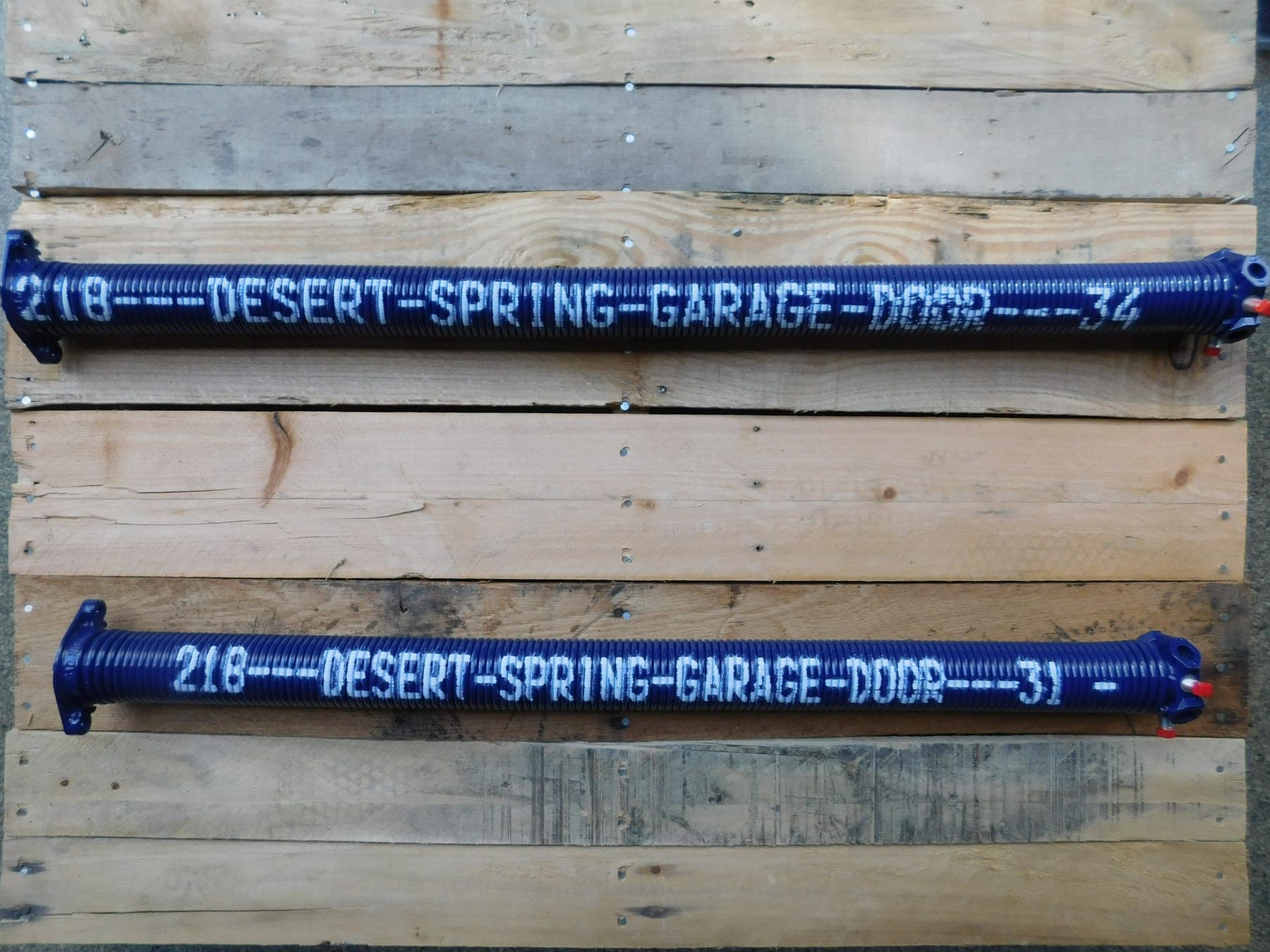 Two custom cobalt Desert Spring Performance Springs on a wood pallet, powder-coated and stenciled DESERT SPRING GARAGE DOOR with their exact sizes